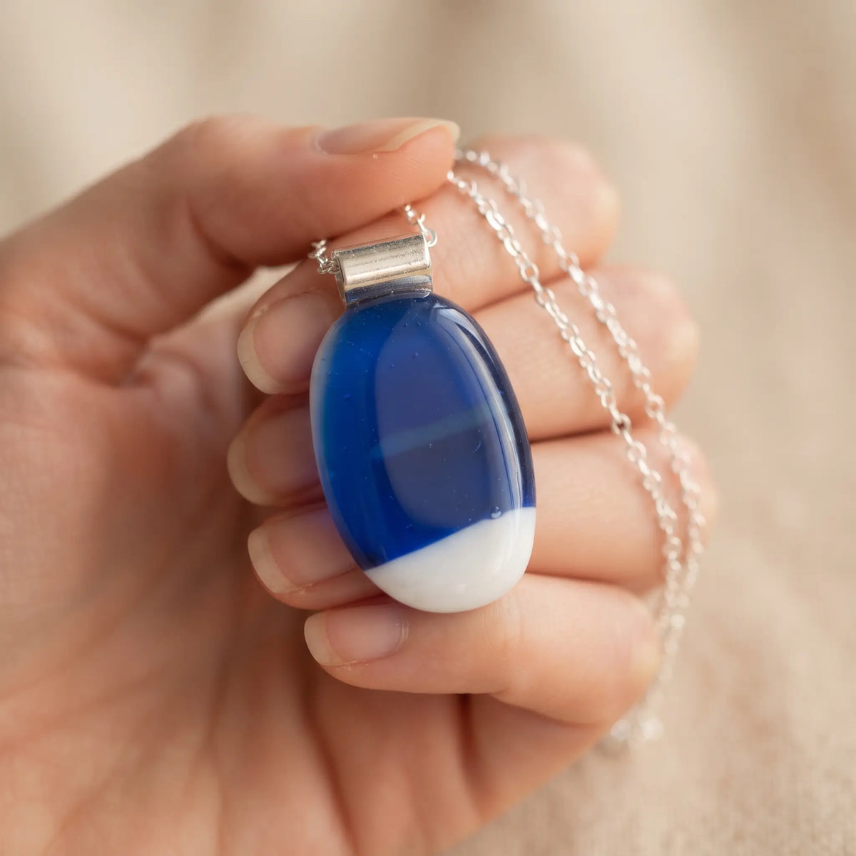Santorini handmade fused glass pendant in deep cobalt blue and white, held in an open palm
