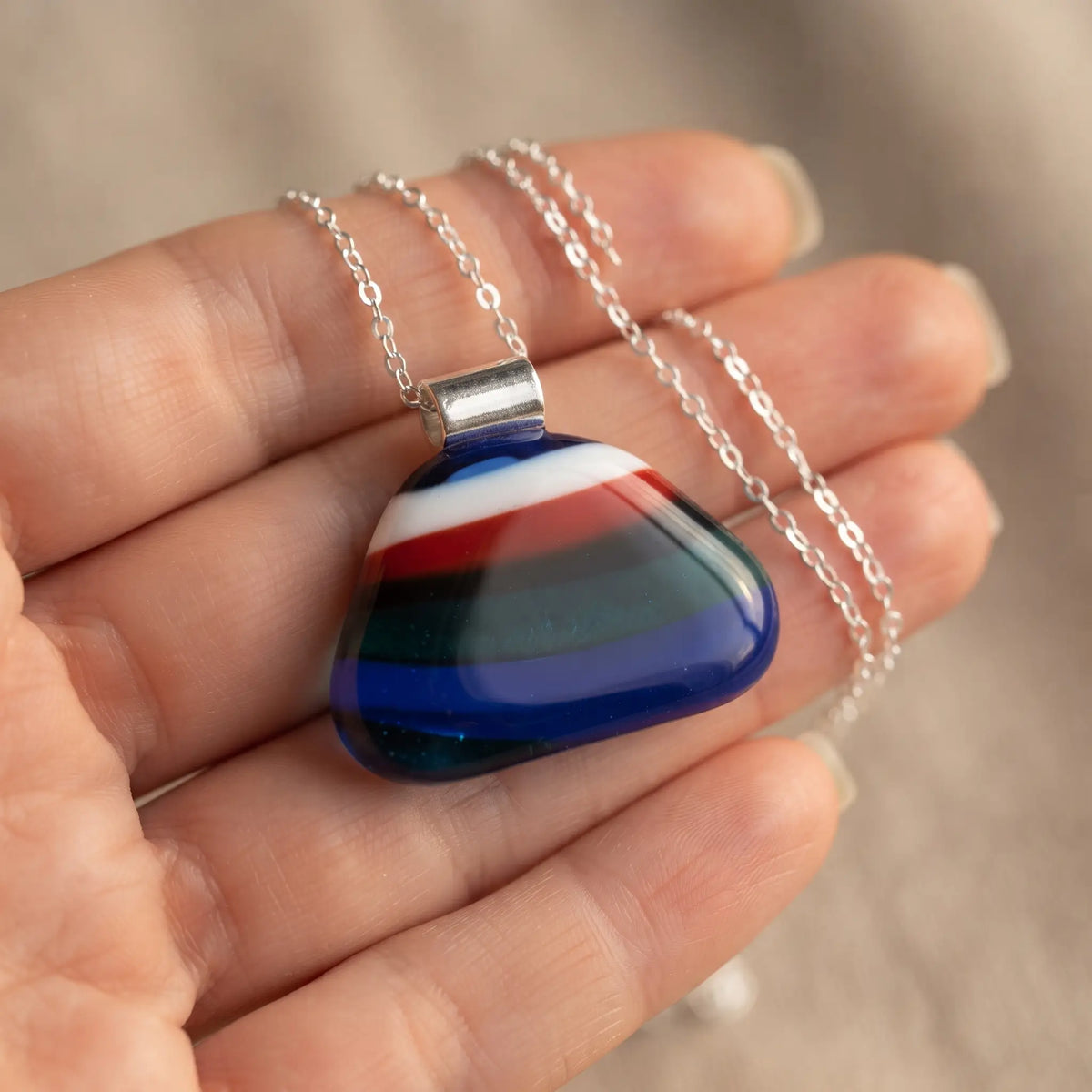 Kingfisher handmade fused glass pendant in royal blue, red, teal, white and black, held in an open palm