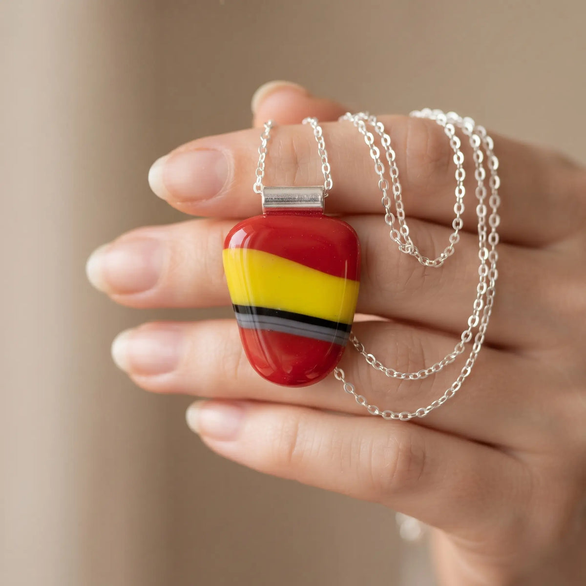Carmen handmade fused glass pendant in glossy red with bright yellow, black and grey, held in an open palm