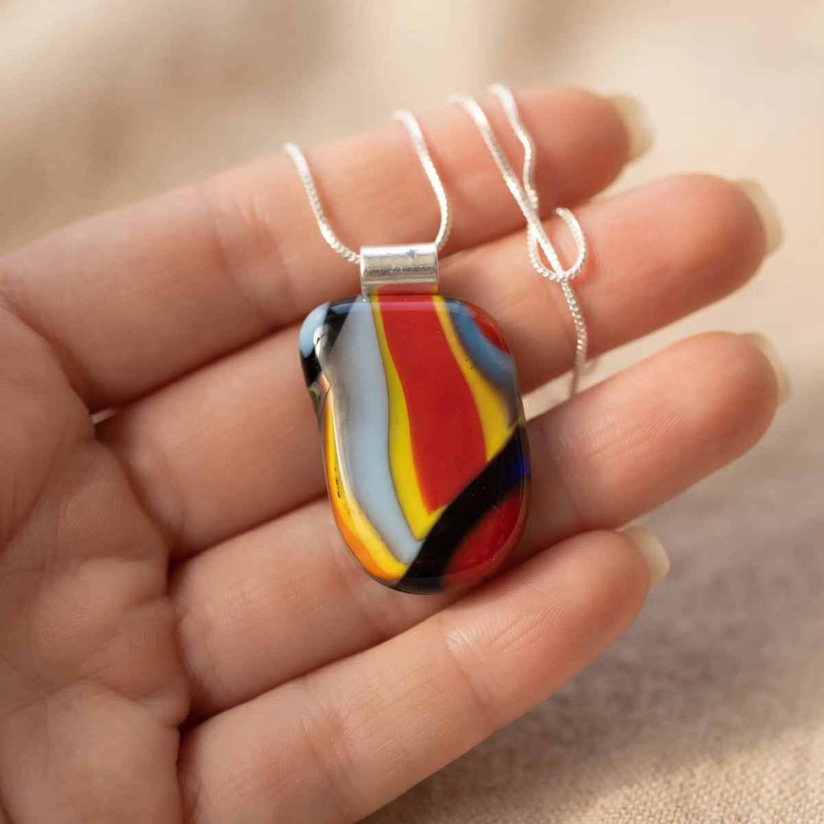Kandinsky handmade fused glass pendant in red, yellow, orange, cobalt and black swirls, held in an open palm
