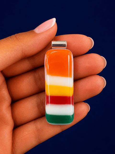 Harvest Stripe handmade fused glass pendant in tangerine orange, sunshine yellow, cherry red, white and teal green, held in an open palm