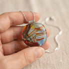 Brushstroke handmade fused glass pendant in deep red, burnt orange, pale blue and aqua, held in an open palm