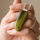 Malachite handmade fused glass pendant in deep forest green and olive with chartreuse threads, held in an open palm