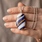 Regimental Stripe handmade fused glass pendant in cobalt blue, white, golden amber, black and caramel, held in an open palm